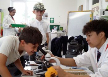 An older pupil helps a young visitor to use a microscope at the STEM fair. Picture courtesy of Evendons Primary School